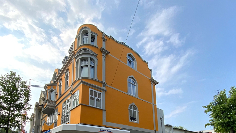 Gelbes Altbaugebäude mit weißen Fensterrahmen und historischer Fassade unter blauem Himmel.